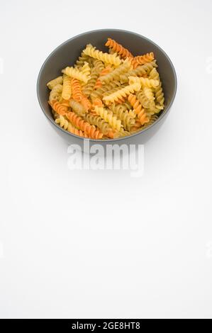 Colpo verticale di pasta rotini tricolore su una ciotola isolata su sfondo bianco Foto Stock