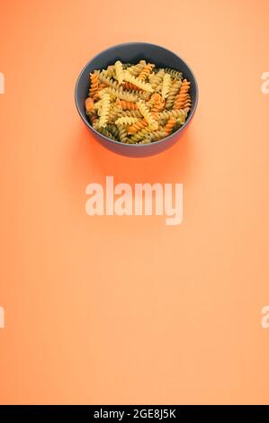 Colpo verticale di pasta rotini tricolore su una ciotola isolata su sfondo arancione Foto Stock