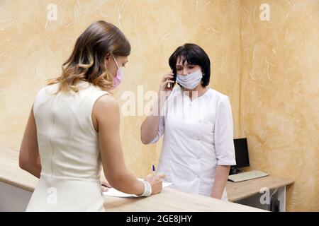 Giovane donna firma carta al banco della reception in maschera di faccia Foto Stock