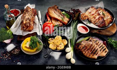 Assortimento di carne di maiale alla griglia con verdure su sfondo grigio scuro. Concetto di cibo gourmet biologico. Foto Stock