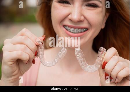 Bella giovane donna dai capelli rossi con bretelle sui denti che tengono i fermi rimovibili all'aperto Foto Stock