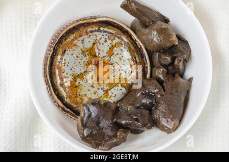 Il botulismo, il pericolo di avvelenamento da cibo per concetto di cibo in scatola. Funghi marinati non adatti in una ciotola bianca in ceramica. Coperchio in stagno arrugginito con macchia nera Foto Stock