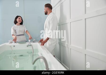 Donna in uniforme mostra bagno idromassaggio per l'ospite uomo in un salone moderno Foto Stock