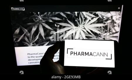 Persona che detiene il telefono cellulare con il logo della società americana di cannabis PharmaCann Inc. Sullo schermo di fronte alla pagina web aziendale. Mettere a fuoco sul display del telefono. Foto Stock