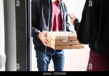 Consegna pizza a domicilio. Ordine online con telefono. Cliente che utilizza l'app mobile per smartphone per pagare, mancia o dare valutazione e revisione. Liberatore domestico. Foto Stock