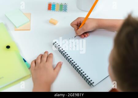 Formazione online a distanza. Bambino ragazzo studiando a casa con il libro, scrivendo in blocco note e facendo i compiti della scuola. Bambini che si siedono al tavolo con Foto Stock