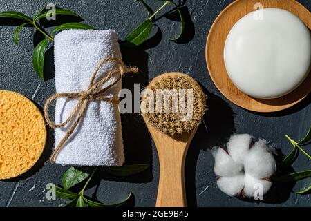 SPA Accessori naturali organici per il trattamento del viso e del corpo con fiori di cotone e foglie verdi su sfondo nero. Niente rifiuti essenziali per il bagno, p Foto Stock