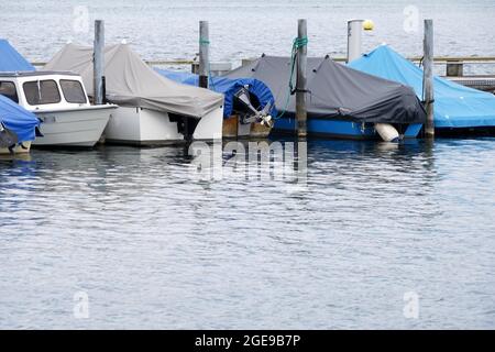 Barche a vela disposte in fila coperte per la stagione invernale e con vele abbassate. Le navi si ancorano sul lago di Zug, nella città di Zug, in Svizzera. Foto Stock