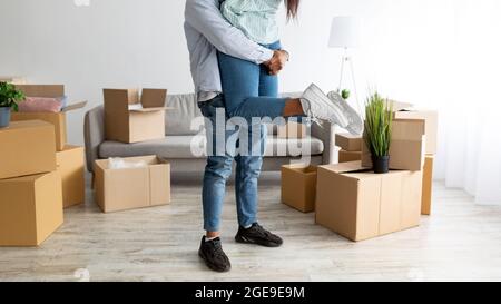 Spostarsi in casa propria. Amore marito nero sollevare sua moglie e divertirsi tra le scatole in nuovo appartamento, raccolto Foto Stock