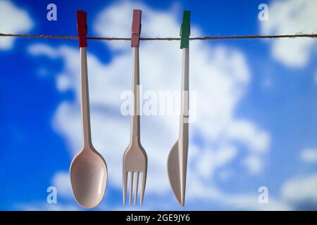 Cucchiaio di plastica, forchetta e coltello appesi ad asciugare con cielo blu e nuvole bianche sullo sfondo. Foto Stock