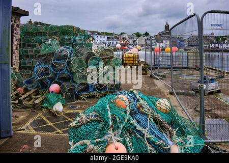 In un pomeriggio grigio e coperto, reti da pesca e pentole di aragosta fiancheggiano il lato della banchina a Tarbert Foto Stock