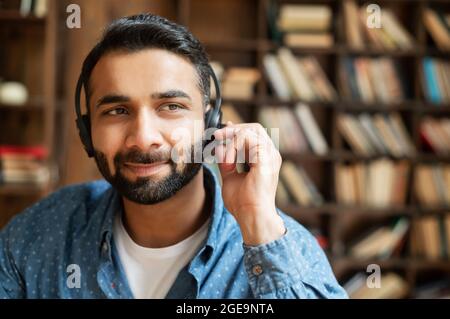 La testa di un dipendente indiano maschio che indossa cuffie auricolari prende una chiamata, parla con clienti o colleghi, un rappresentante del supporto interno, la testa di un addetto del call center indù che tocca le cuffie Foto Stock
