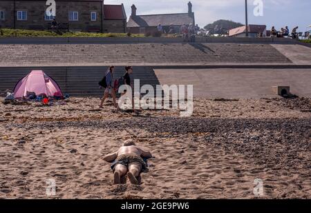 Uomo che prende il sole sulla spiaggia di sabbia a Whitby in Inghilterra. Foto Stock