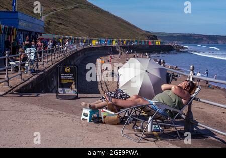 Donna che si rilassa sulla sdraio sulla spiaggia a Whitby in Inghilterra. Foto Stock