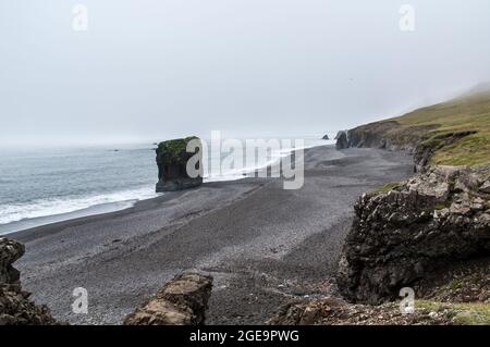 Bellissimo scatto di scogliere rocciose su una spiaggia in Islanda in una giornata di nebbia Foto Stock
