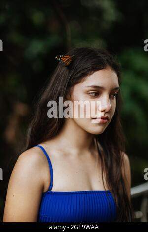 Tranquilla giovane femmina in bikini con farfalle ornamentali sui capelli in piedi contro il verde offuscato fogliame durante l'avventura estiva in Costa Rica Foto Stock
