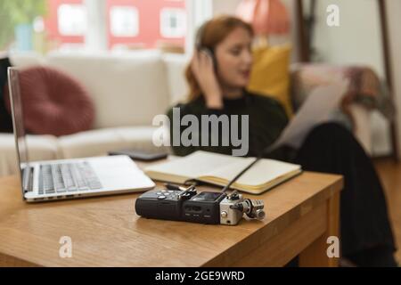 Moderno registratore audio posto su tavolo di legno sullo sfondo di blurred radio host femminile in cuffie registrazione podcast Foto Stock