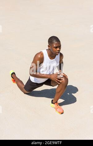 Fit atleta africano americano maschio facendo affondo esercizio e allungare le gambe mentre si riscalda durante l'allenamento in estate soleggiato giorno Foto Stock