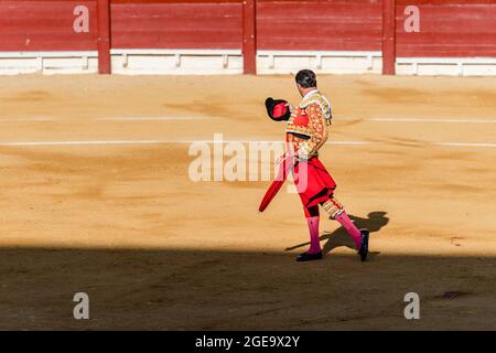 Vista posteriore di un irriconoscibile bullfighter in costume fantasia che prende il cappello dopo lo spettacolo di corrida mentre ci si trova su un'arena di sabbia Foto Stock