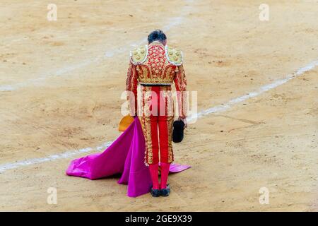 Vista posteriore di un irriconoscibile bullfighter in costume fantasia che prende il cappello dopo lo spettacolo di corrida mentre ci si trova su un'arena di sabbia Foto Stock