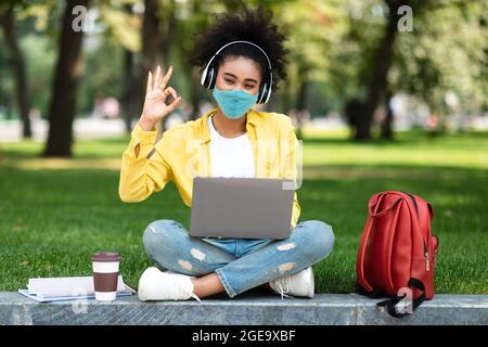 African Student Girl usando il laptop che indossa maschera gesturing bene all'aperto Foto Stock