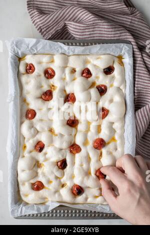 Dall'alto di persona anonima che decorano l'impasto per una deliziosa focaccia con pomodori secchi Foto Stock