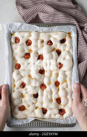 Dall'alto di persona anonima che decorano l'impasto per una deliziosa focaccia con pomodori secchi Foto Stock