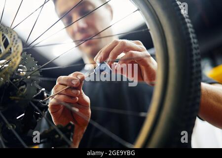 uomo in maglietta nera che si avvita nella ruota mentre fissa la bicicletta in garage Foto Stock