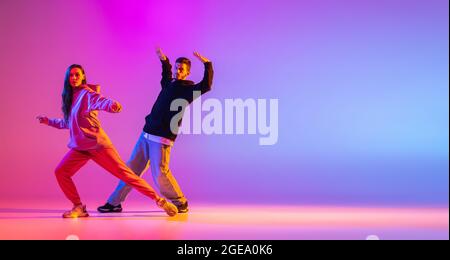 Volantino. Due giovani, un ragazzo e una ragazza che ballano la danza contemporanea, hip-hop su sfondo rosa con luce al neon. Foto Stock