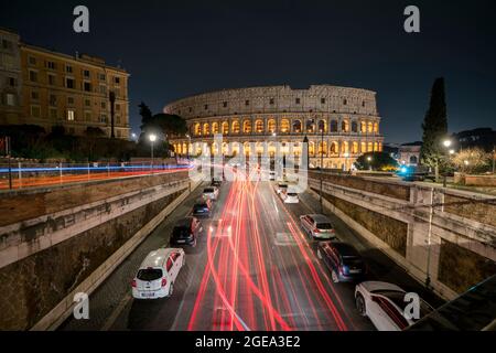 Il traffico dipinge sentieri leggeri mentre passa oltre il Colosseo di Roma in Italia. Foto Stock