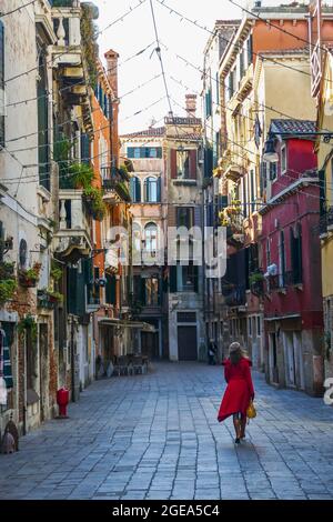 Una donna in un petticoat rosso e beretto passeggiano lungo le incantevoli strade di Venezia. Foto Stock
