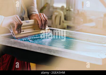 produzione serigrafia. serigrafia tessile serigrafia printery. stampa serigrafica manuale studio di progettazione. foto mani maschili con spatola Foto Stock