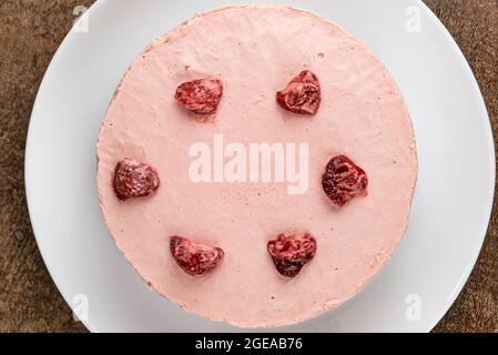 Vista dall'alto della deliziosa cheesecake fatta in casa con fragole secche guarnite in piastra di ceramica bianca su tavola di legno scuro. Foto Stock