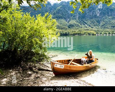 Donna bionda in piedi nel lago di Bohinj, accanto ad una barca sulla spiaggia Foto Stock