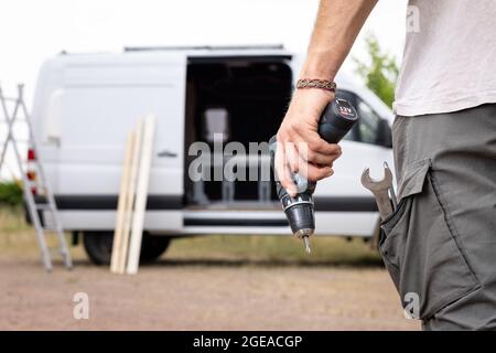 Cacciavite elettrico tenuto da una mano e un furgone sullo sfondo Foto Stock