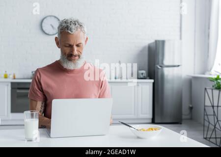 Freelancer maturo che usa un computer portatile vicino alla colazione in cucina Foto Stock