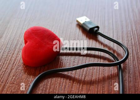 Cuore rosso con cavo usb su sfondo in legno. Amore e concetto di tecnologia Foto Stock