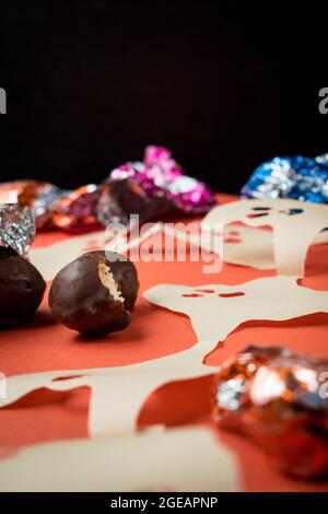 Alcuni cioccolatini, diversi involucri colorati e fantasmi di carta sulla superficie arancione Foto Stock