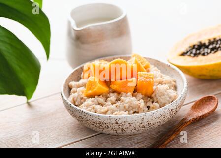 Farinata d'avena con frutta tropicale papaya su un tavolo di legno. Colazione sana Foto Stock