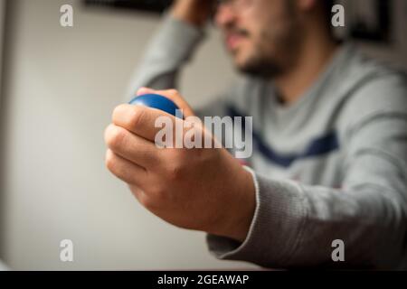 L'uomo stressato con gli occhiali , stringendo la pallina blu da stress e graffiando la testa Foto Stock