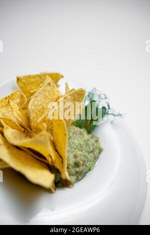 closeup di guacamole immersione in ciotola con avocado e nachos su sfondo bianco Foto Stock