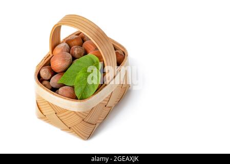 La nocciola si trova in un cestino di legno su uno sfondo bianco isolato. Nocciole non pelate in guscio e foglie verdi Foto Stock