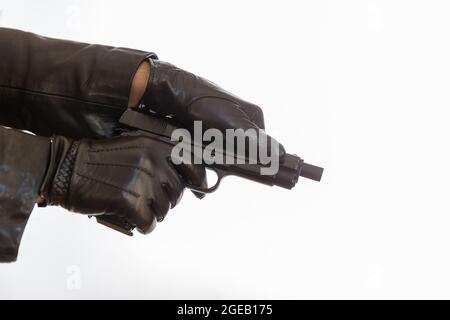 Uomo gustato armando la sua pistola. Killer indossando guanti in pelle con una pistola che si prepara a sparare isolato su sfondo bianco, vista closeup. Arma da fuoco, Foto Stock