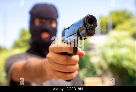 Burglar con balaclava, tenendo una pistola. Uomo che punta con una pistola, natura all'aperto sfondo, vista closeup. Concetto di intruso, ladro armato Foto Stock