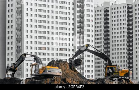 Gli escavatori lavorano sul terreno sullo sfondo di case a più piani Foto Stock