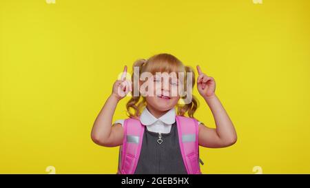 Bambino della ragazza della scuola in uniforme che mostra i pollici in su, indicando in su allo spazio della copia per il soddisfare promozionale Foto Stock