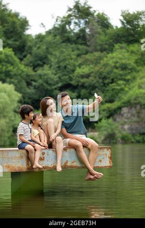 Felice giovane famiglia cinese che prende selfie con smartphone al molo Foto Stock