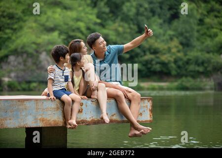 Felice giovane famiglia cinese che prende selfie con smartphone al molo Foto Stock