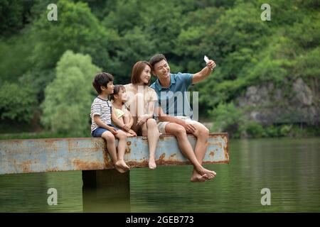 Felice giovane famiglia cinese che prende selfie con smartphone al molo Foto Stock