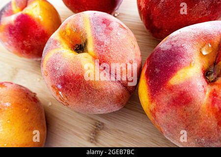 Pesche biologiche mature su un tagliere con pelle rossa e gialla vivace Foto Stock